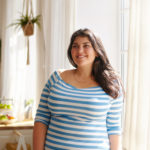 Beauty, bodypositivity, people and lifestyle concept. Indoor shot of gorgeous brunette Latin girl posing by window in kitchen dressed in xxl blue and white striped shirt, having joyful beaming smile
