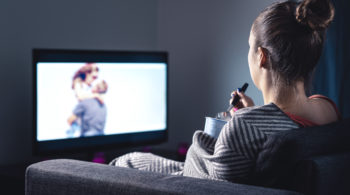 Woman watching romantic movie and eating ice cream. Sad lonely single girl streaming series or film on tv home at night. Person with stream on television.